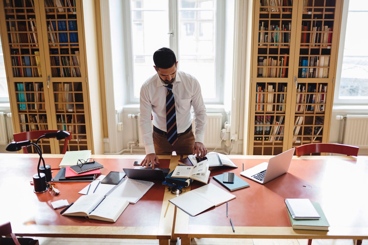 man researching while standing at table in home library